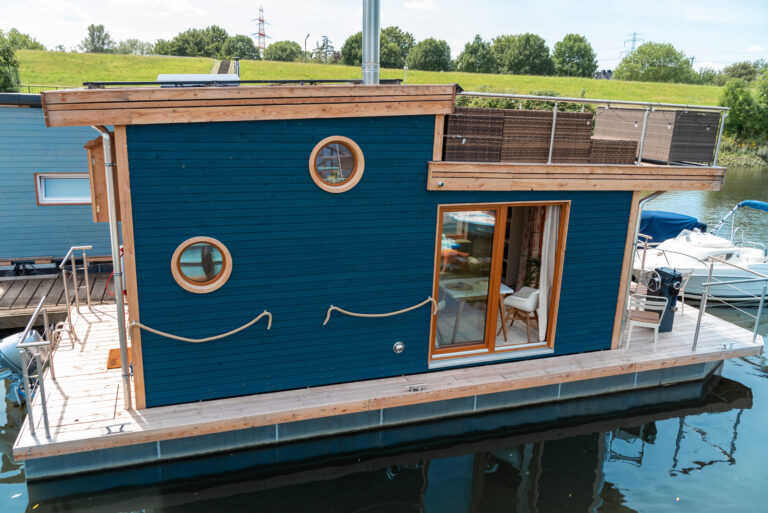 Tiny-Hausboot IRENE, nach ökologischen Maßstäben gebaut und 2023 fertiggestellt. Frühstücksterrasse vorne, Dachterrasse mit Sitzlounge oben, Holzofen im Innenbereich, gut ausgestattete Küchenzeile, kleines Bad und 2-4 Schlafplätze.