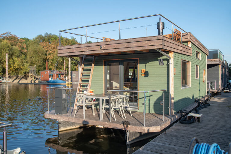 Aussenansicht bugseits des grünen Hausboots Petite an einem Anleger im Diamantgraben bei Sonnenschein.